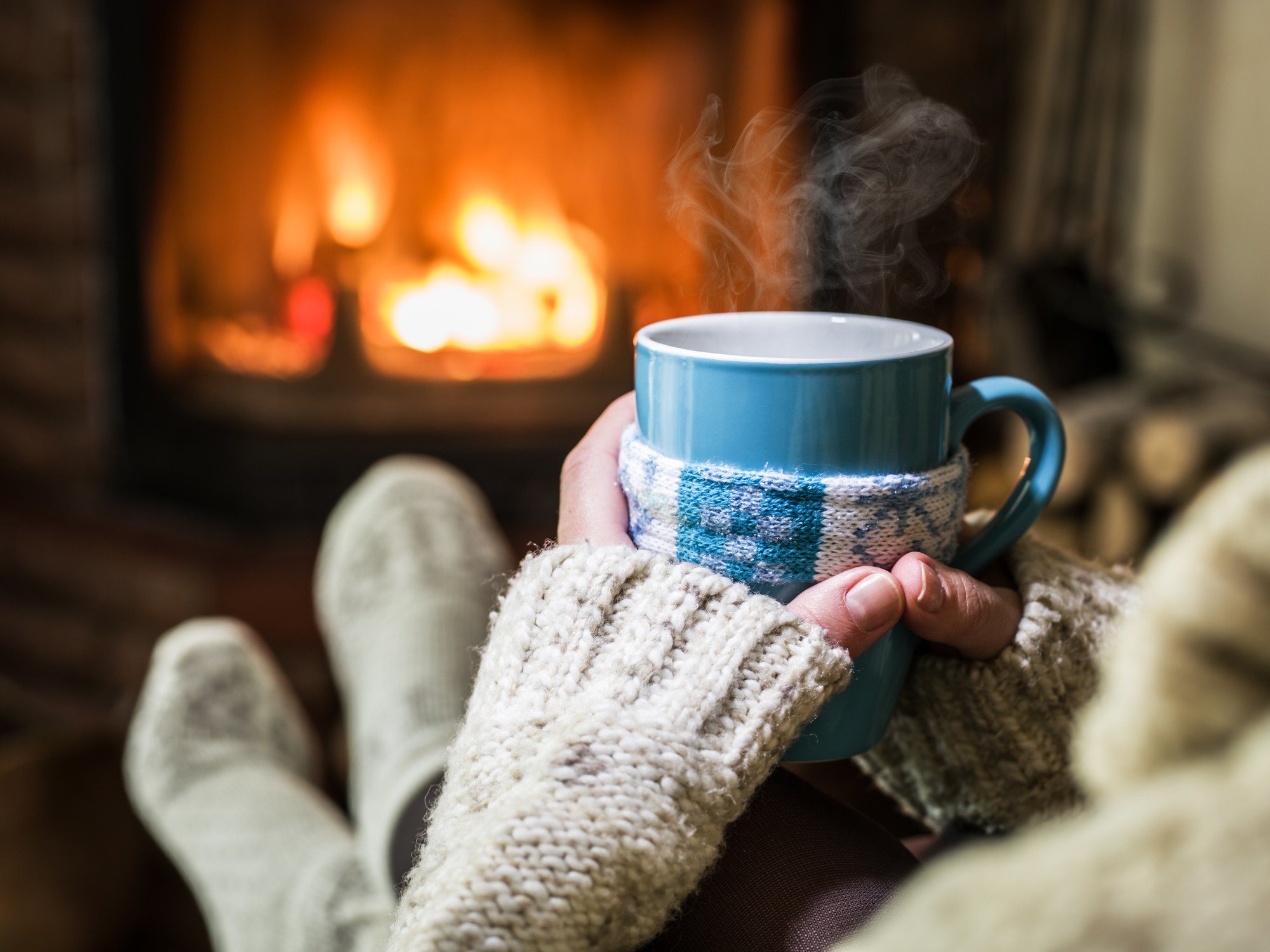 Person Holding Hot Cup of Coffee by a Fireplace
